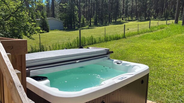 Een hottub op een houten terras, met een gazon en bomen op de achtergrond.