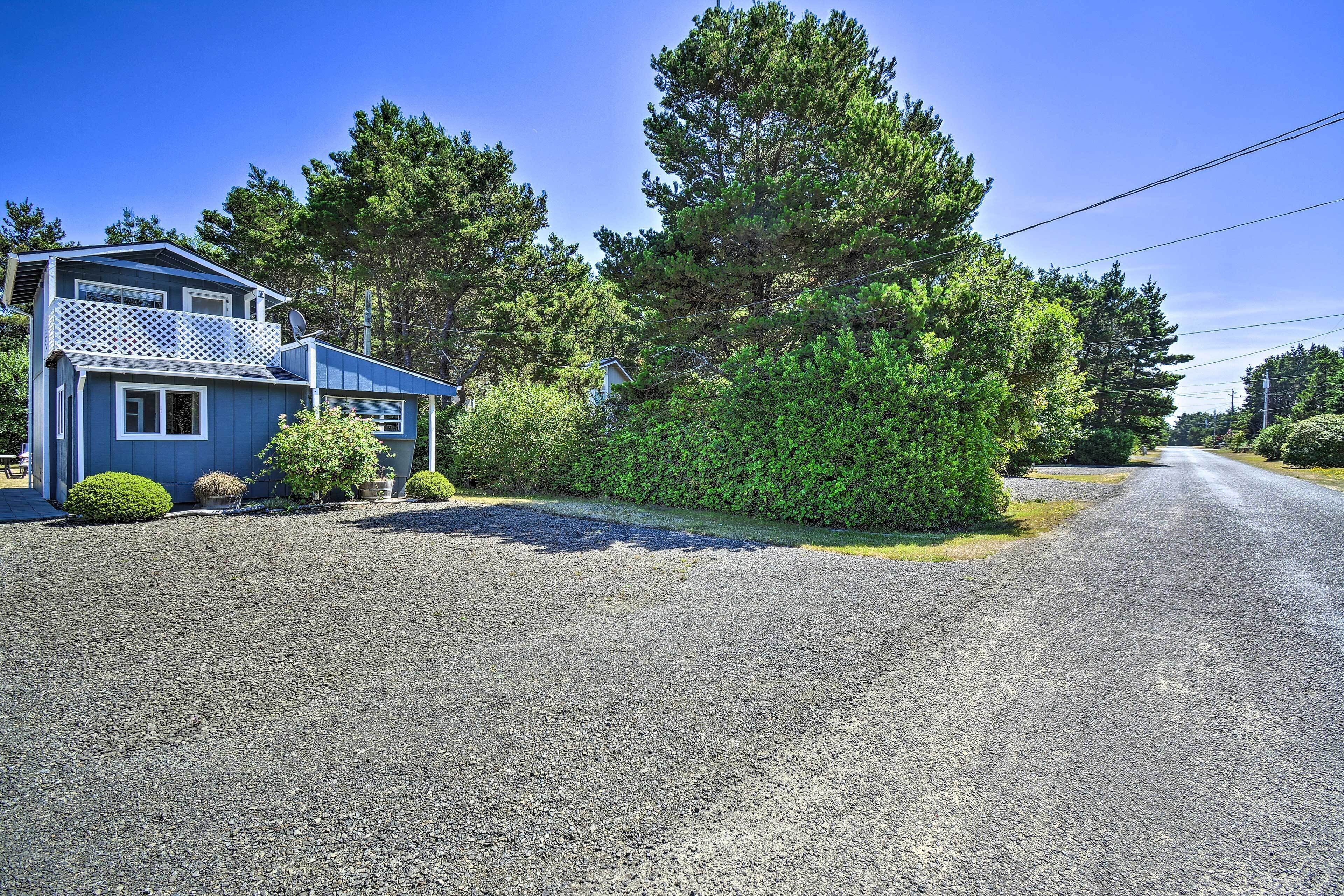 A two-story house with a balcony, surrounded by dense greenery and a gravel driveway.