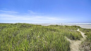 Ein Küstenpfad, der zum Meer führt, mit grasbewachsenen Dünen.