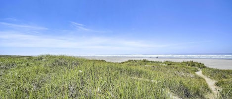 A beach path leading to the ocean with grassy dunes.
