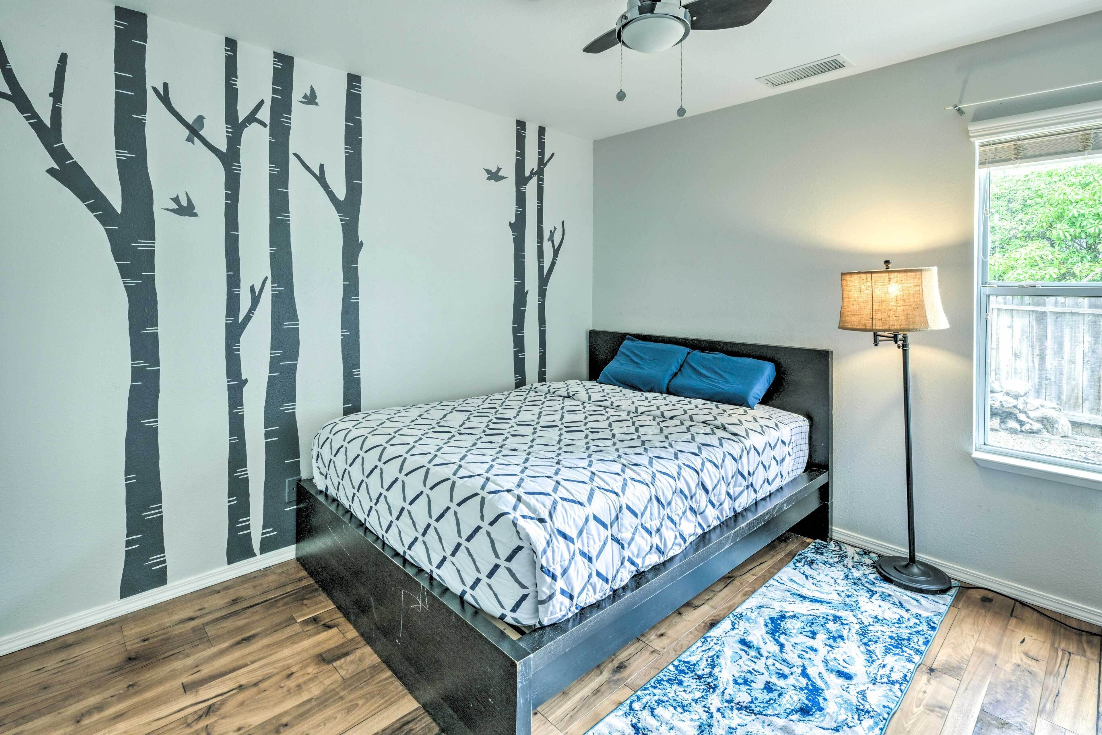A bedroom with a bed, a floor lamp, a window, and a wall with tree decals.