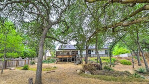 Una casa amb terrassa, envoltada d'arbres i un pati curt i sec.