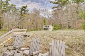 A wooden deck with two Adirondack chairs and a small cabin in a wooded area.