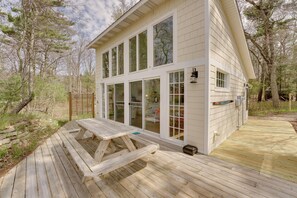 A wooden deck with a picnic table, a house with large windows, and a wooden fence.