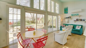 A bright room with large windows, a ceiling fan, a white table with red chairs, and a teal sofa. - Beachfront Lake Michigan Cottage: Fire Pit & Deck (Muskegon)