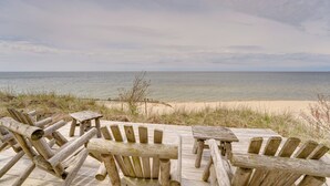 A wooden deck with chairs and tables overlooking a beach. - Beachfront Lake Michigan Cottage: Fire Pit & Deck (Muskegon)