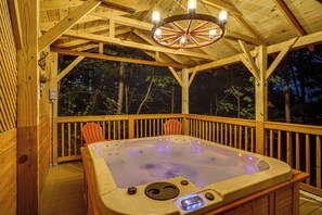 A wooden deck with a hot tub, wooden railings, and a ceiling with a wheel chandelier.