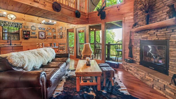 A rustic cabin interior with a wooden dining table, leather sofa, and a stone fireplace. - Bear Mountain Chalet in the Woods w/ Hot Tub (Sevierville)