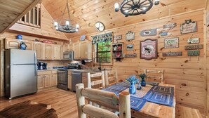 A rustic cabin interior with wooden walls, a dining table with placemats, a refrigerator, and a microwave. - Bear Mountain Chalet in the Woods w/ Hot Tub (Sevierville)