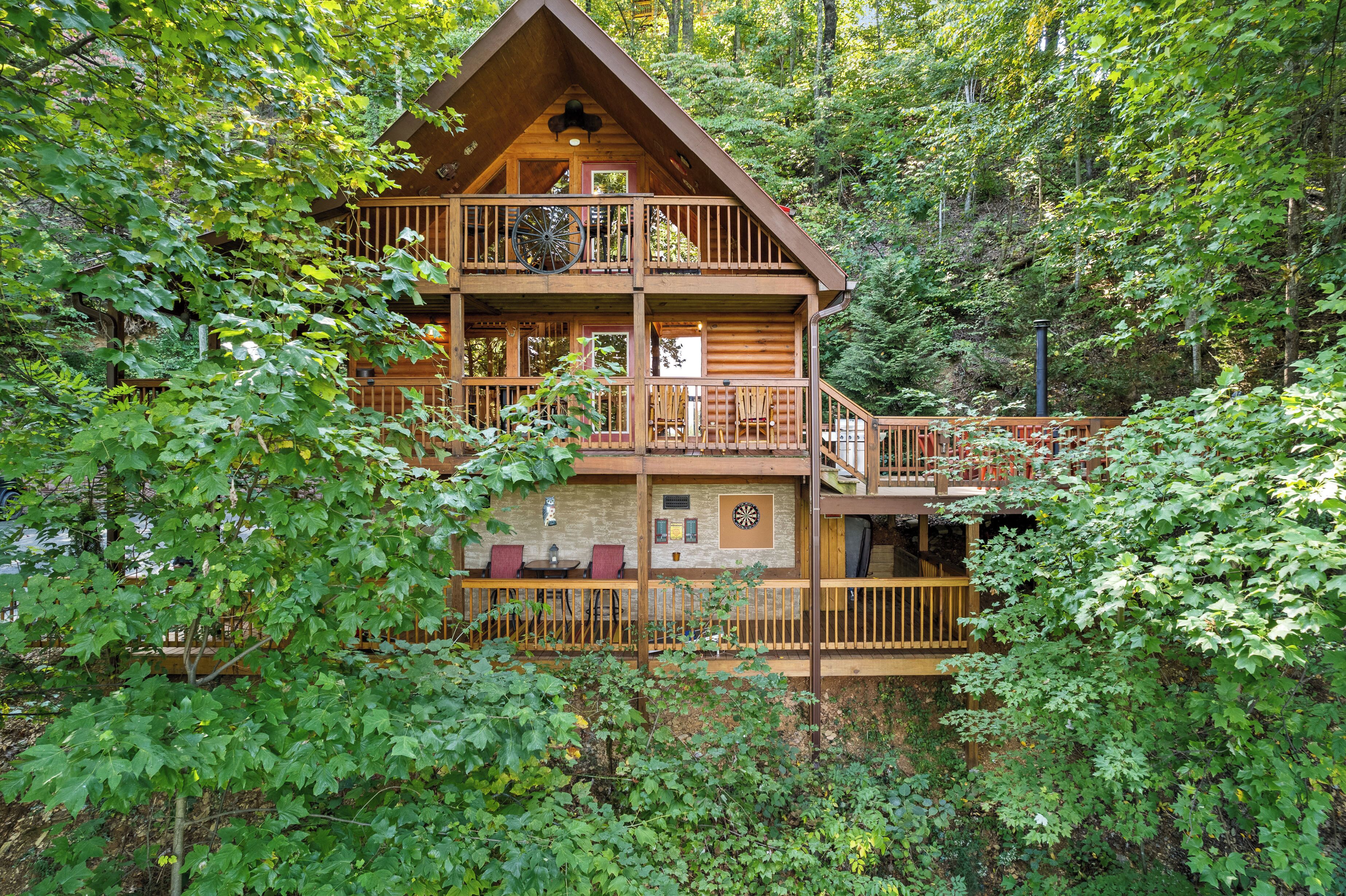 A multi-story log cabin with a balcony, surrounded by dense forest.