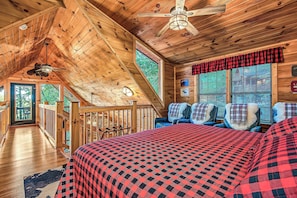A cabin interior with a large bed, a ceiling fan, and a view of the outdoors.