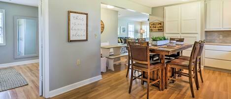 Un comedor con mesa y sillas de madera, una cocina con armarios blancos, y un letrero que dice 'WELCOME TO THE LAKE'.