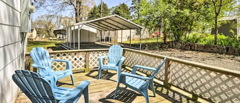 A wooden deck with blue Adirondack chairs and a covered patio area.