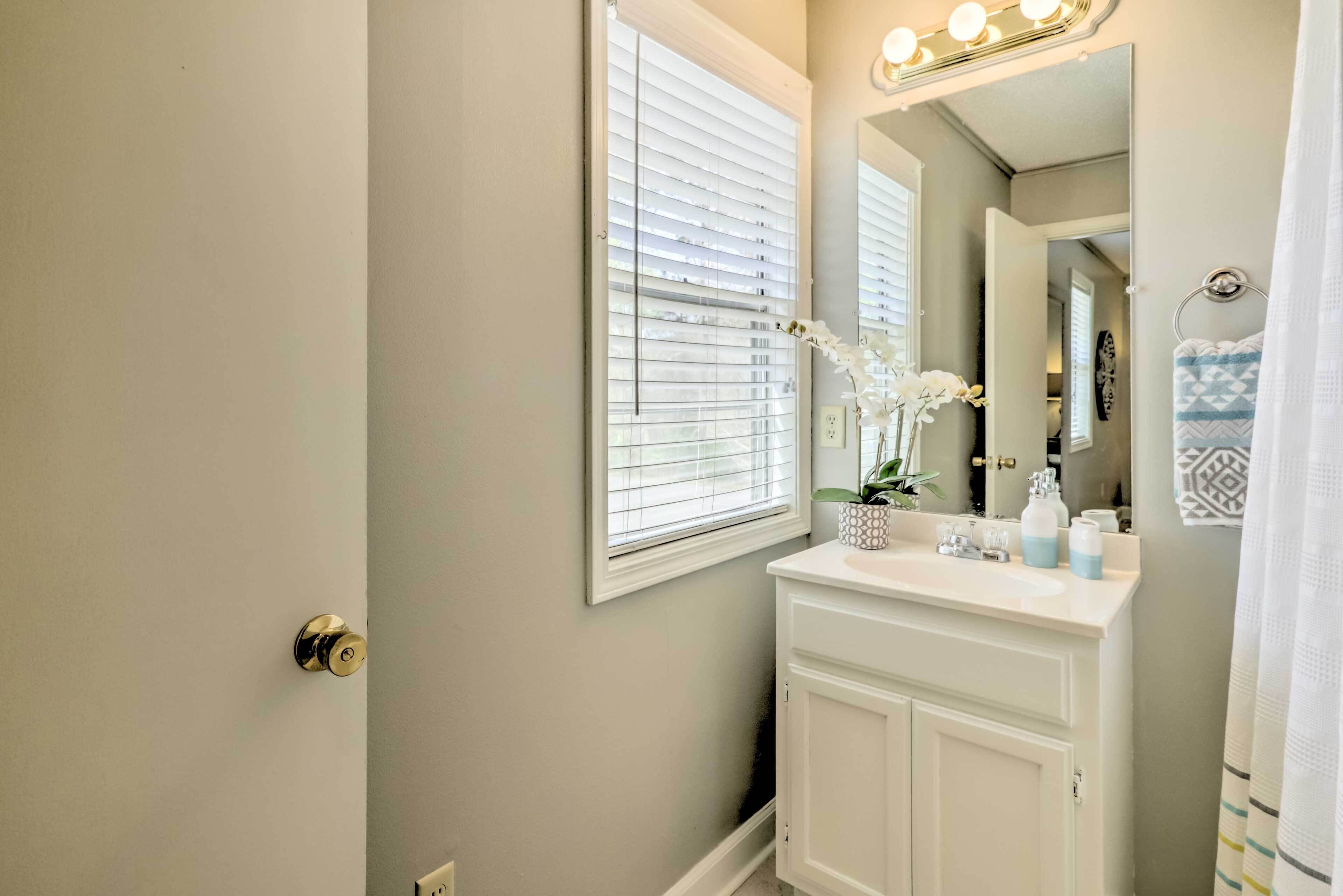 Une salle de bain avec un meuble-lavabo, un miroir et une fenêtre avec des stores.