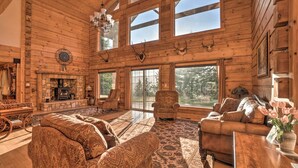 A spacious log cabin interior with a stone fireplace, large windows, and rustic furniture. - Brookings Vacation Rental Lodge on 88 Acres! (Brookings)