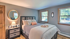 A bedroom with a bed, bedside table, lamp, and a mirror. - Charming Saco Home w/ Deck, 5 Mi to Beach! (Saco)