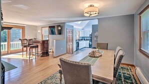 A spacious dining area with a wooden table and chairs, a bar area with stools, and a view into the kitchen. - Charming Saco Home w/ Deck, 5 Mi to Beach! (Saco)