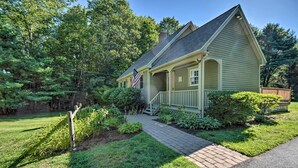 A two-story house with a front porch, a flag, and a well-maintained lawn. - Charming Saco Home w/ Deck, 5 Mi to Beach! (Saco)