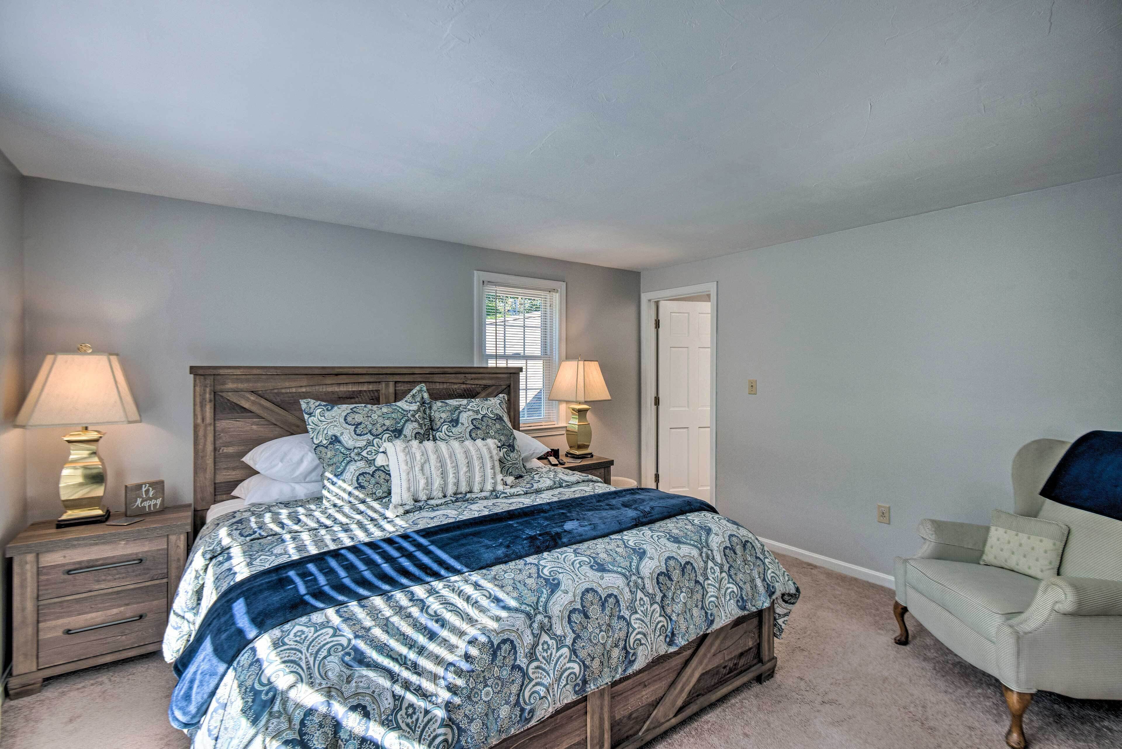 A bedroom with a wooden bed, two bedside tables with lamps, a chair, and a window with blinds.