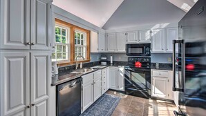 A modern kitchen with white cabinetry, a black countertop, a built-in microwave, a stainless steel refrigerator, and a window with a view of greenery. - Charming Saco Home w/ Deck, 5 Mi to Beach! (Saco)