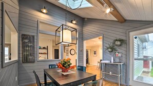 A dining area with a wooden table, chairs, and a hanging light fixture. - Chic Manistee Cottage: Steps to Lake Michigan! (Manistee)