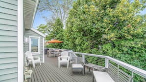 A wooden deck with outdoor furniture, including chairs and a table, and a railing. - Chic Manistee Cottage: Steps to Lake Michigan! (Manistee)