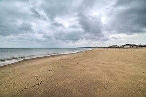 A wide sandy beach with a calm sea and overcast sky.