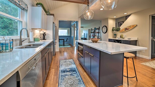 A modern kitchen with wooden floors, a large island, and pendant lighting. - Chic Manistee Cottage: Steps to Lake Michigan! (Manistee)