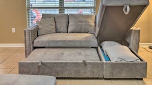 A grey sofa with a pull-out bed, a patterned pillow, and a lamp on the right.