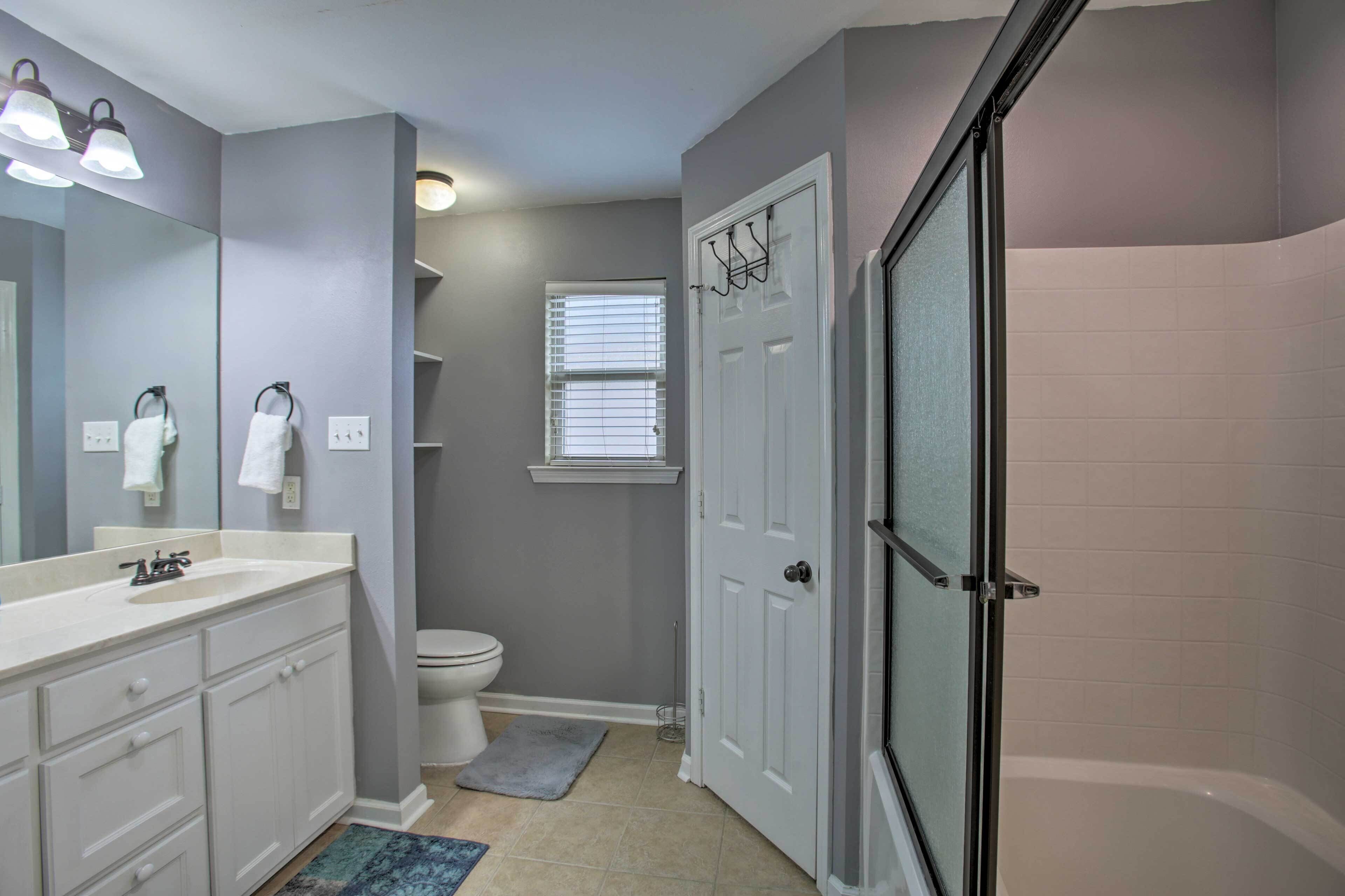A bathroom with a white sink, mirror, and vanity, a toilet, a shower with a glass door, and a window with blinds.