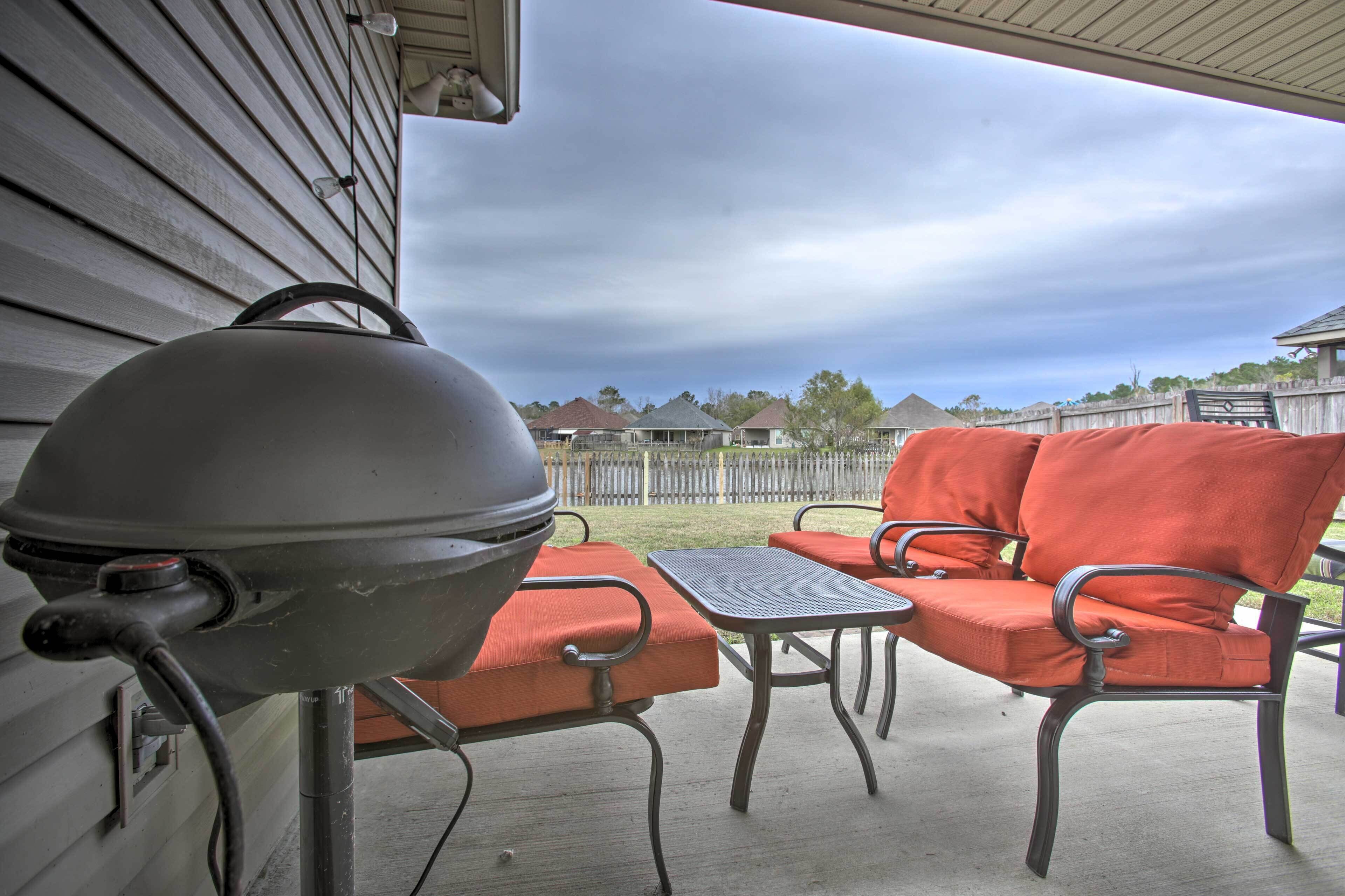A barbecue grill, outdoor seating with orange cushions, and a view of houses in the background.