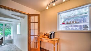 Een houten bureau met een koffiezetapparaat, een raam met uitzicht op een hek, en een deur naar een kamer met een bad.