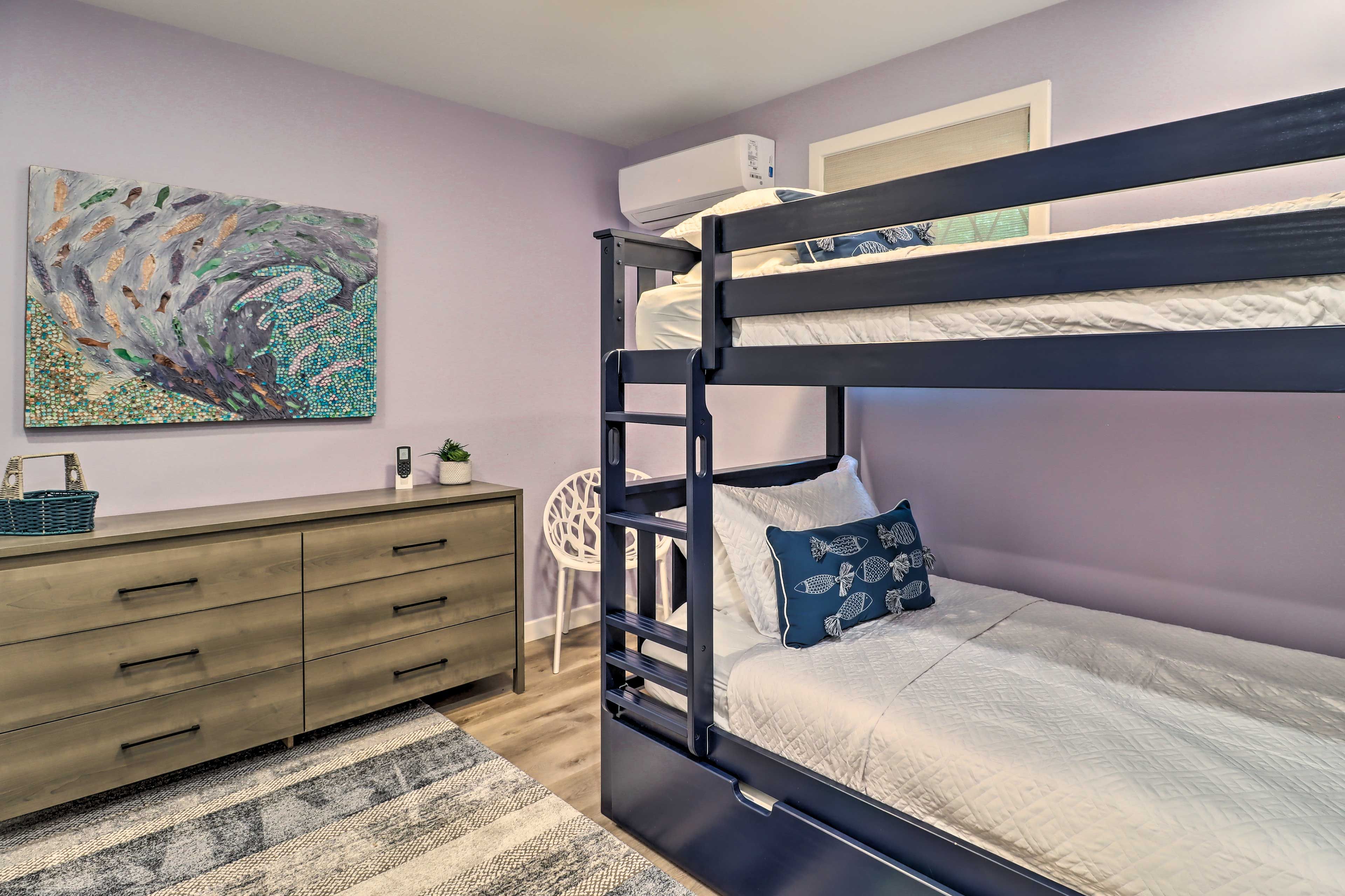 A bunk bed with a headboard, a bedside table, a chair, a wall-mounted air conditioner, and a painting on the wall.