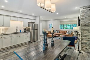 A modern kitchen with white cabinets, a stainless steel refrigerator, and a wooden dining table with blue candle holders.