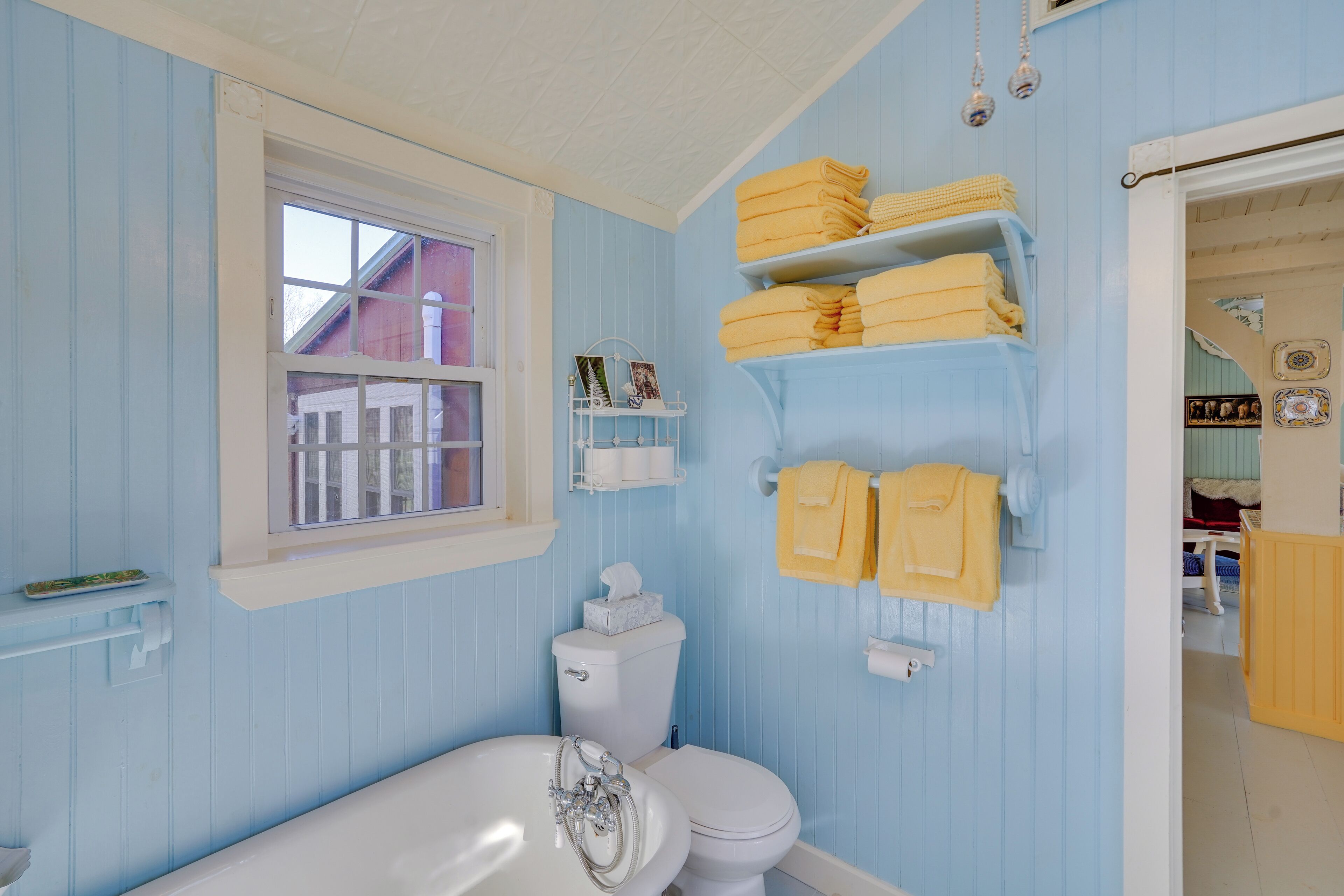 A bathroom with a white bathtub, a toilet, and shelves with yellow towels.