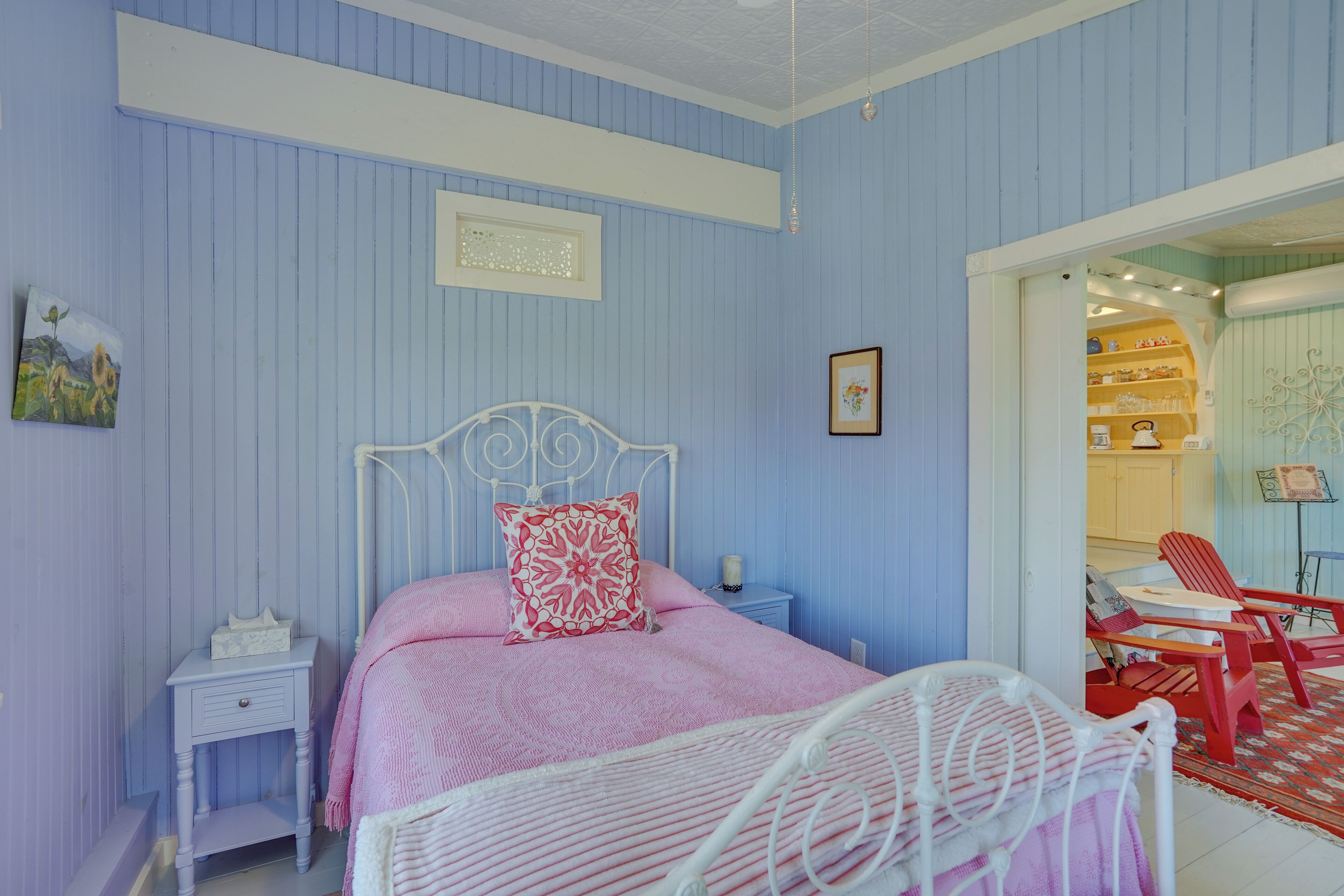 A bedroom with a bed, a nightstand, a chair, and a view into the kitchen.