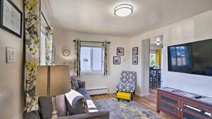 A living room with a sofa, a coffee table, a TV, a patterned chair, and a wooden cabinet. - North Bend Home w/ Cornhole Court & Putting Green (North Bend)