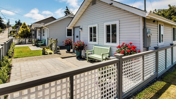 A row of white single-story houses with a fenced patio area, a bench, and potted plants. - North Bend Home w/ Cornhole Court & Putting Green (North Bend)