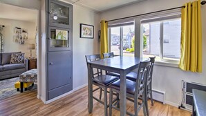 A dining area with a table and chairs, a gray cabinet with glass doors, a sofa, and a window with yellow curtains. - North Bend Home w/ Cornhole Court & Putting Green (North Bend)