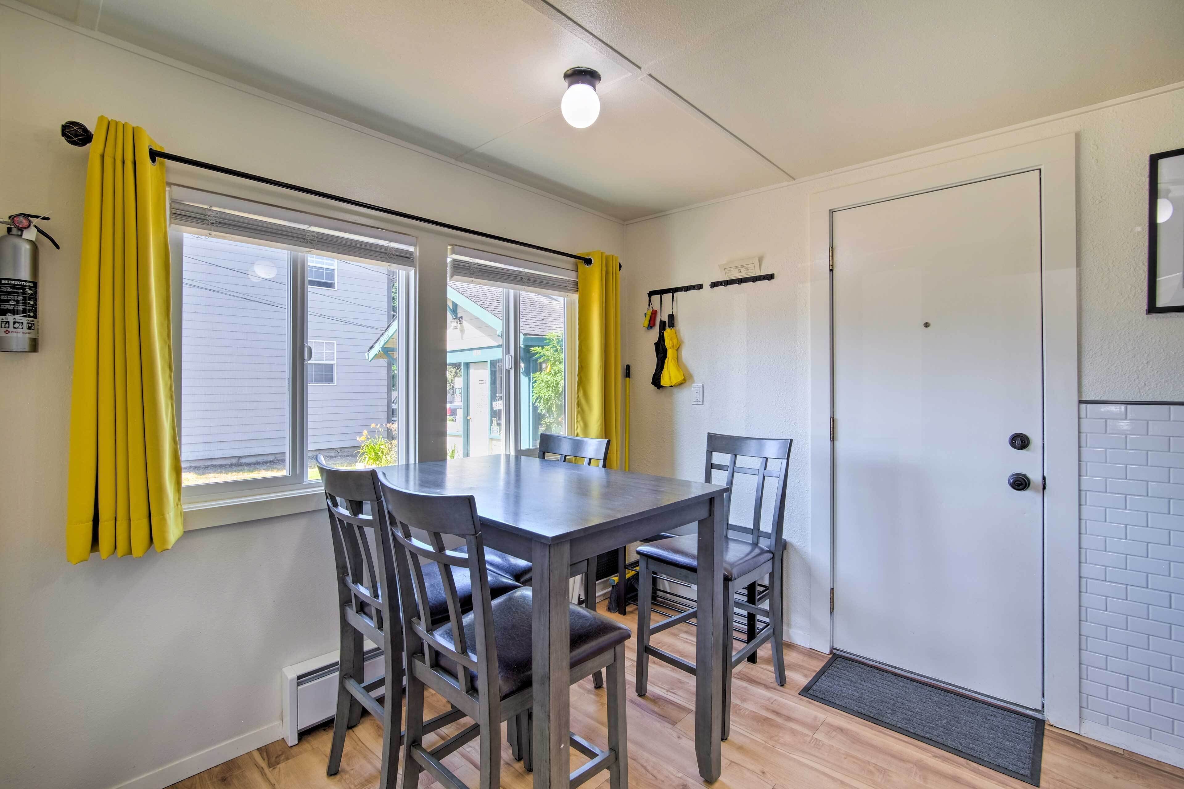 A dining area with a table and chairs, a window with yellow curtains, a white door, and a fire extinguisher on the wall.