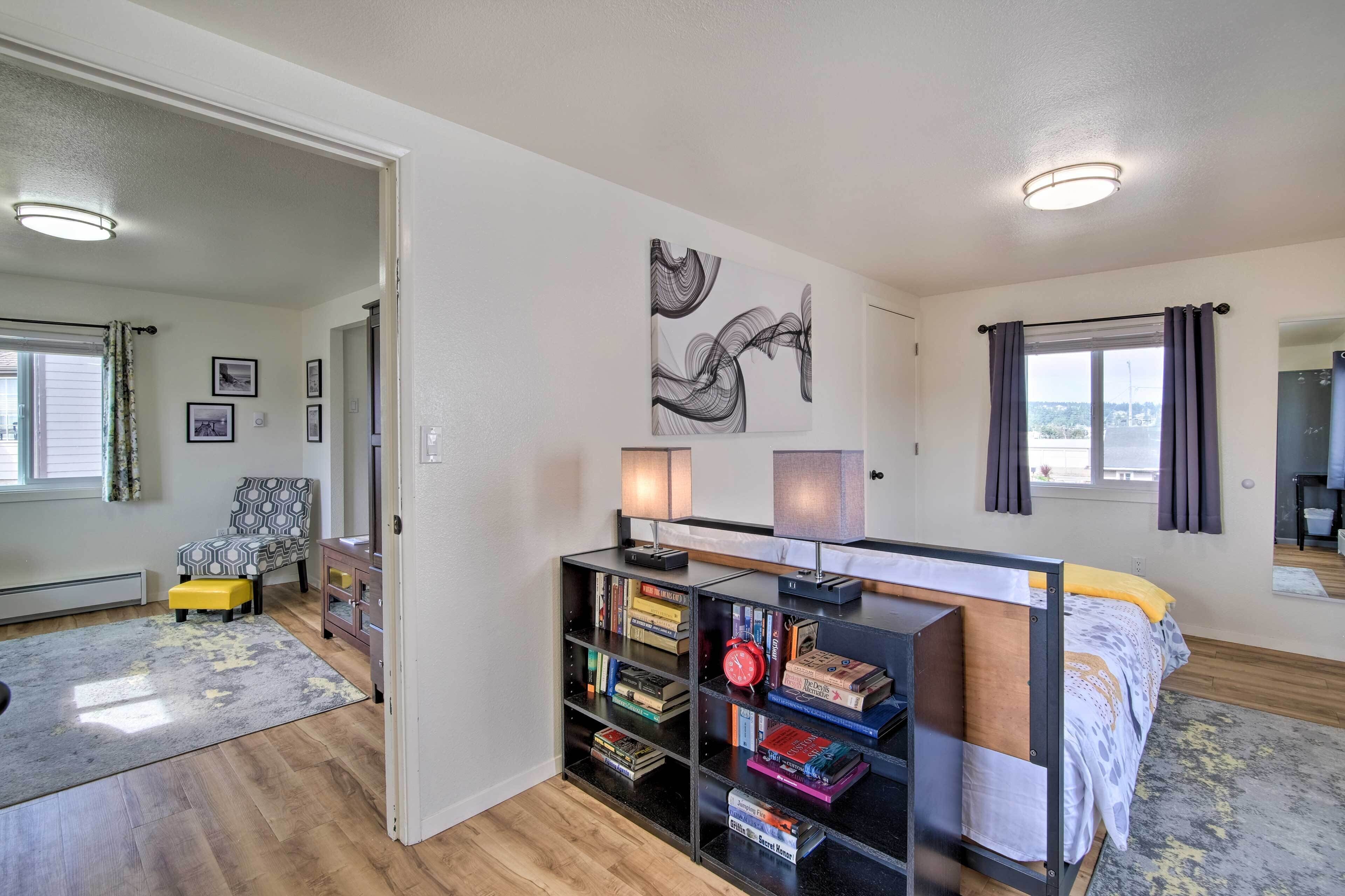 A modern bedroom with a bed, bookshelves, a desk, and a large window.