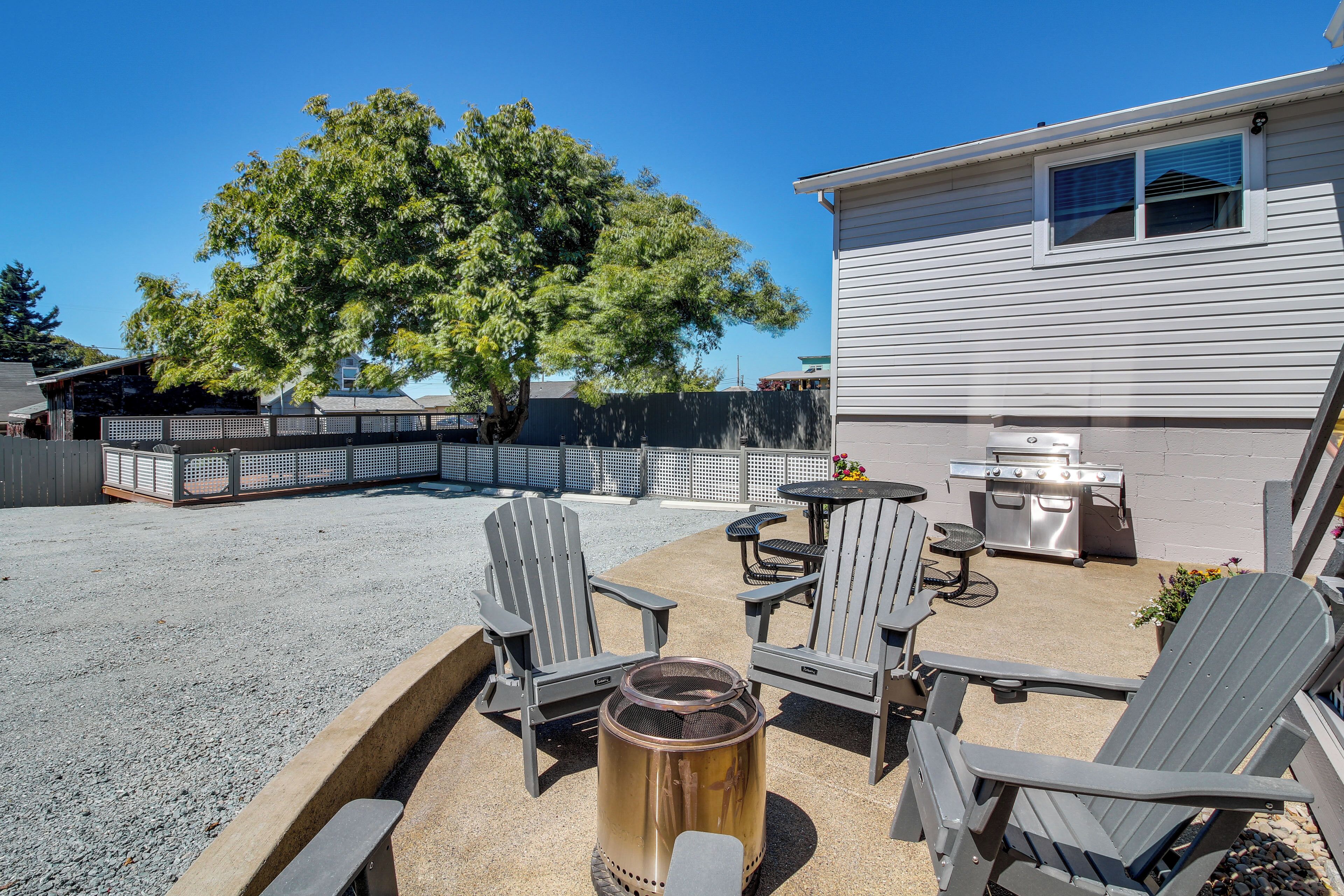 Un patio exterior con sillas Adirondack, una parrilla y un hogar para fuego.