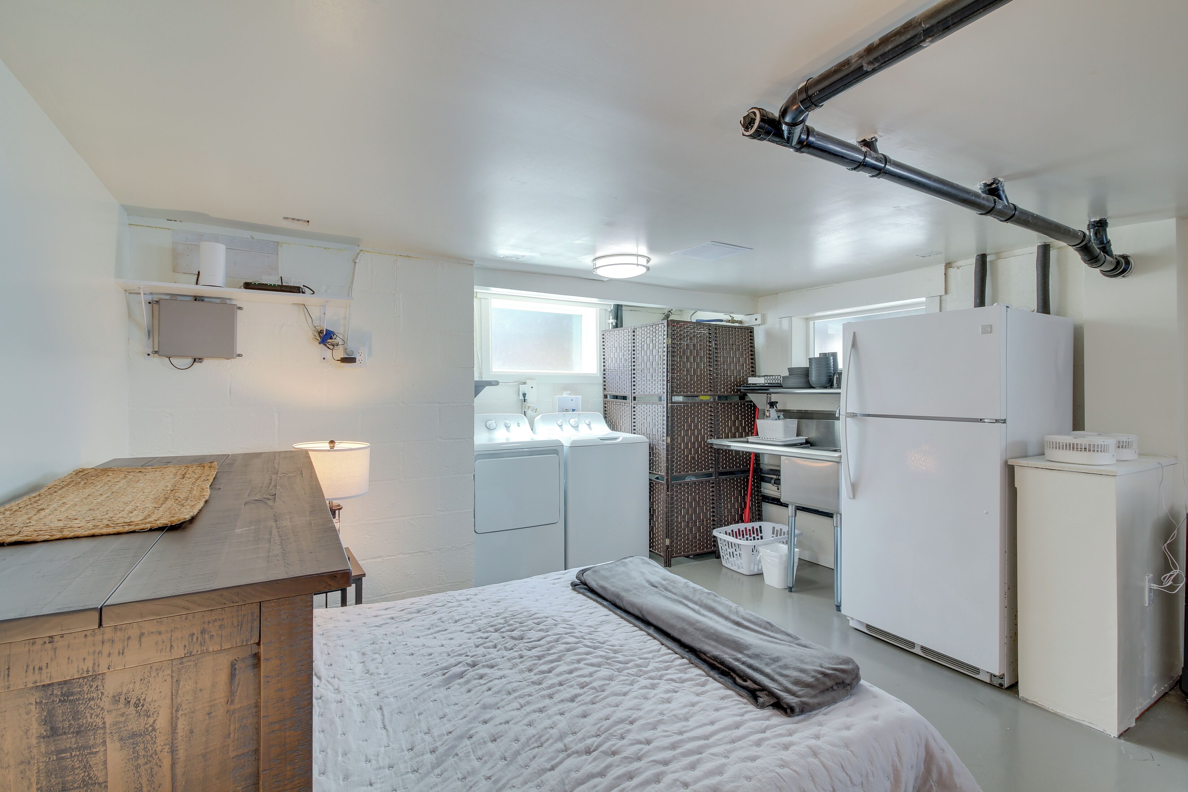 A compact, modern kitchen with a built-in washer and dryer, a refrigerator, and a dining area with a wooden table and bench.