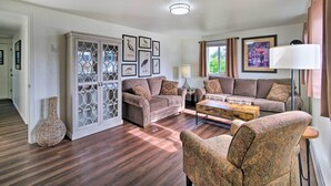 A living room with a sofa, armchairs, a coffee table, and a cabinet with framed pictures. - North Bend Home w/ Cornhole Court & Putting Green (North Bend)