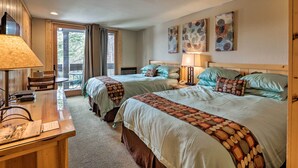 A hotel room with two beds, a desk, and a chair. There are two windows with curtains, a door, and artwork on the wall. - Condo at Northstar Village - Base of Ski Resort! (Truckee)