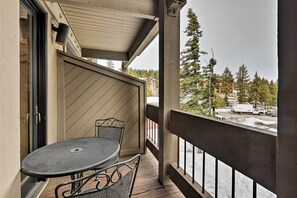 A balcony with a table and chairs, a wooden railing, and a view of a snowy landscape with trees and buildings in the background.