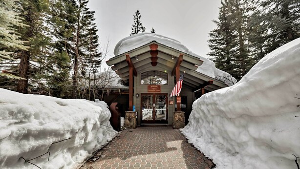 A snow-covered entrance to a lodge with a brick pathway leading to a wooden structure with a sign reading "Welcome to N. D. O. S. Recreation Center." - Condo at Northstar Village - Base of Ski Resort! (Truckee)