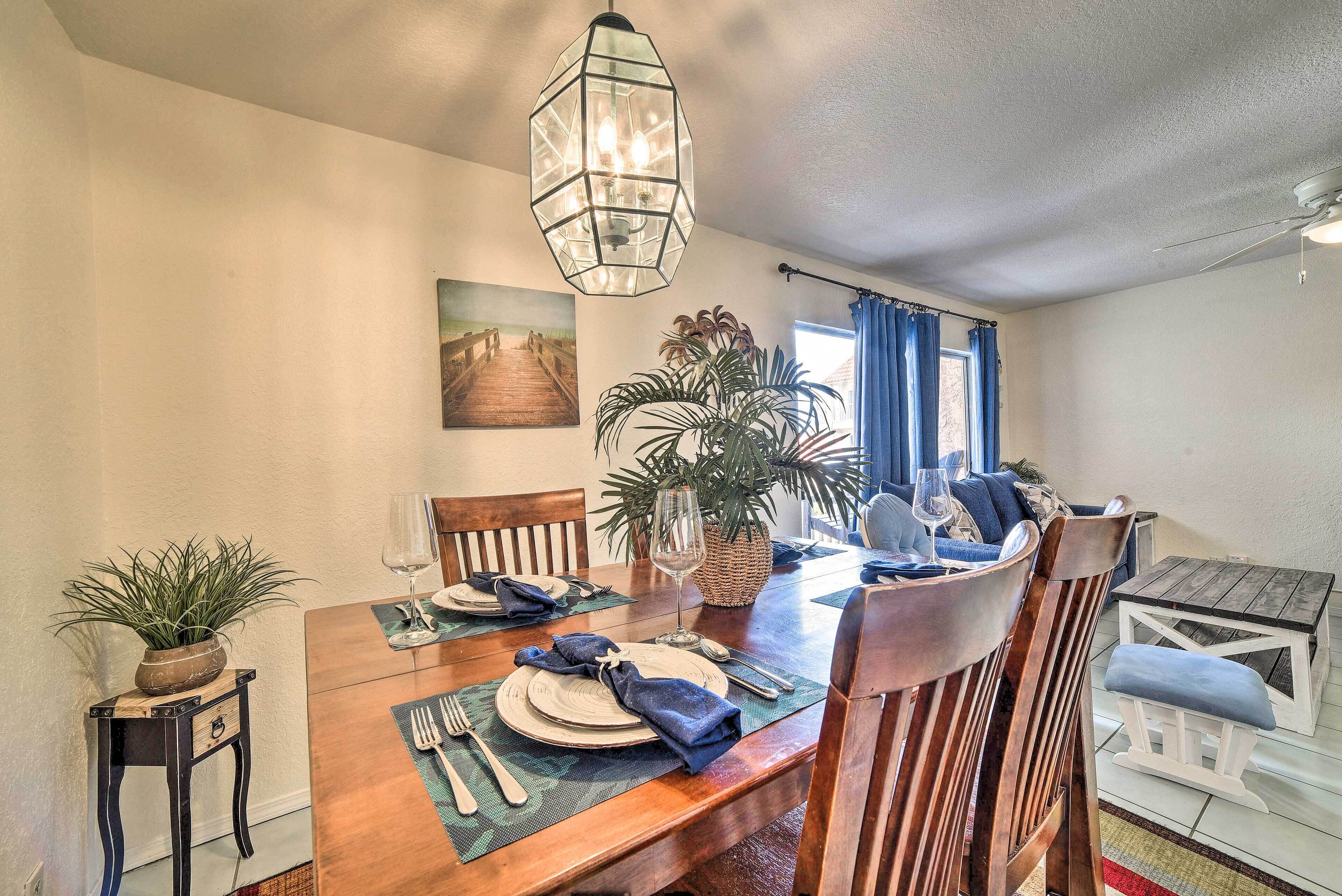 A dining area with a wooden table set for four, a hanging light fixture, and a large potted plant.