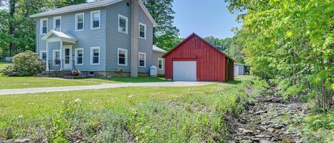 A two-story house with a red barn, a front porch, and a well-maintained lawn.