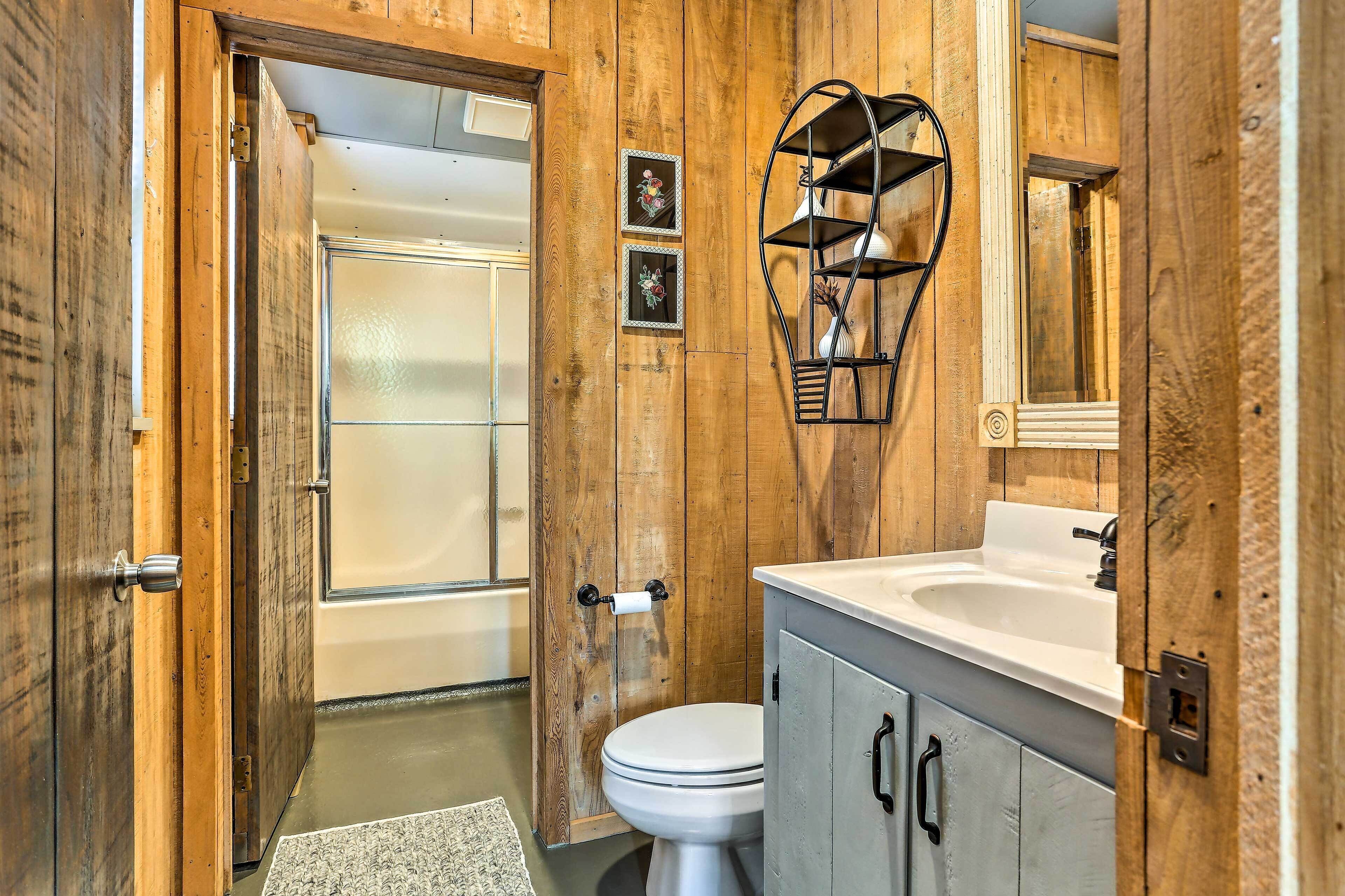 A wooden-paneled bathroom with a toilet, sink, and shower.